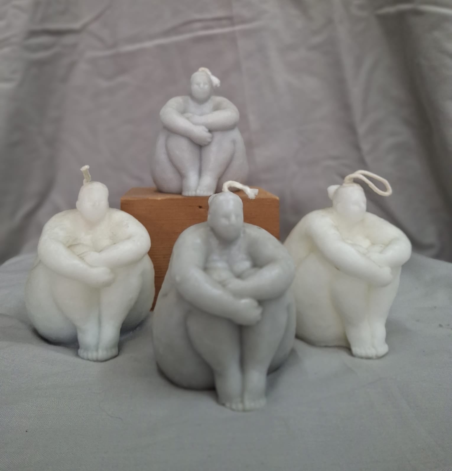 Sculpted candles in grey and white depicting serene, seated feminine figures with arms wrapped around their legs — symbolizing calm, self-acceptance, and inner peace.