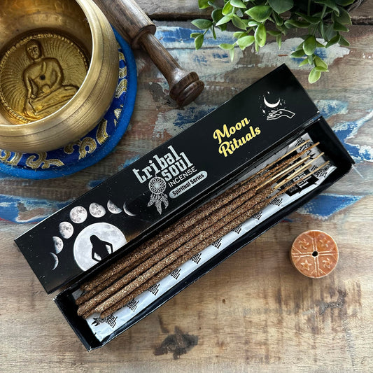 A box of Tribal Soul Moon Rituals incense sticks displayed alongside a bronze singing bowl, a wooden yoga block, and a small circular incense holder with a design.