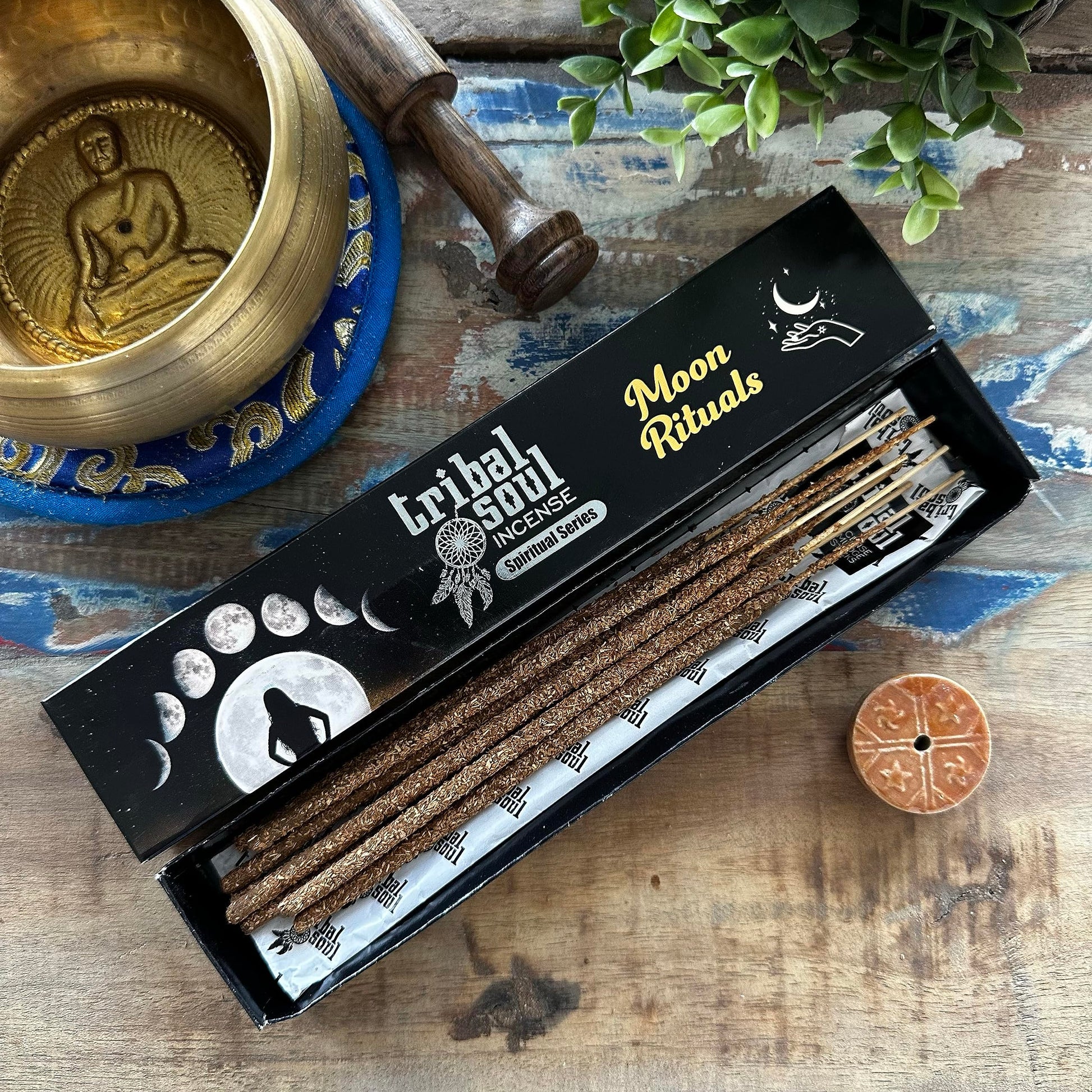 A box of Tribal Soul Moon Rituals incense sticks displayed alongside a bronze singing bowl, a wooden yoga block, and a small circular incense holder with a design.