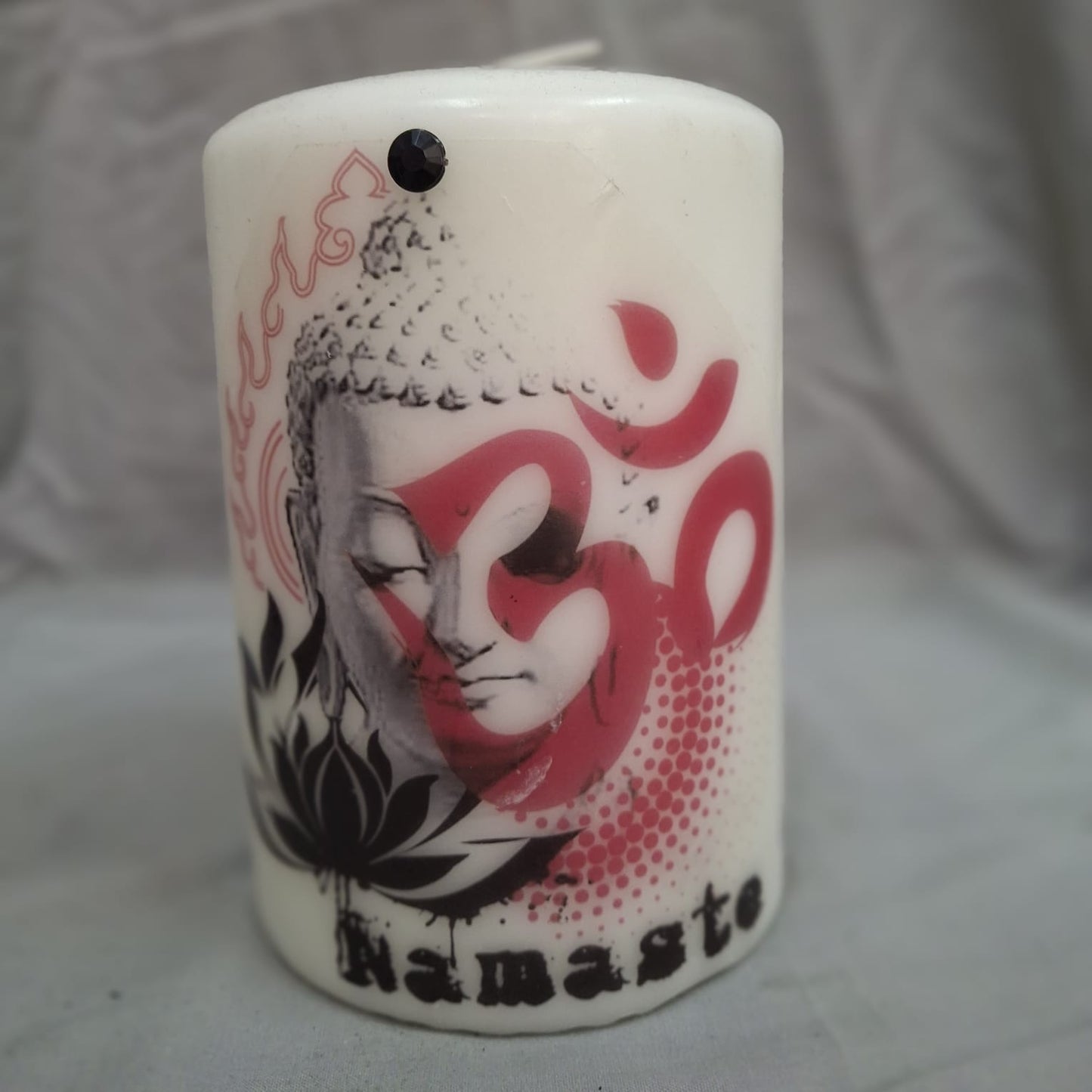 White decorative candle with Buddha face, red Om symbol, and Namaste