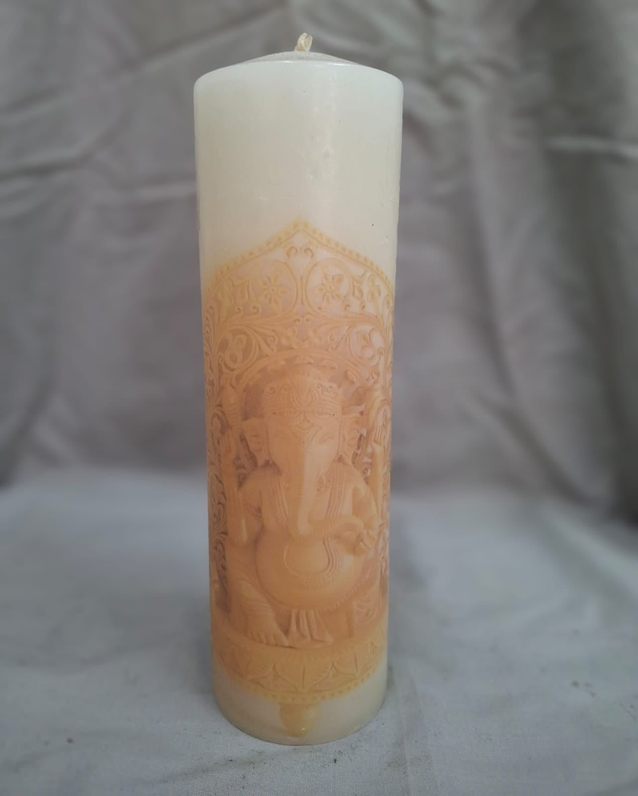 White decorative candle with orange Lord Ganesha design and patterns